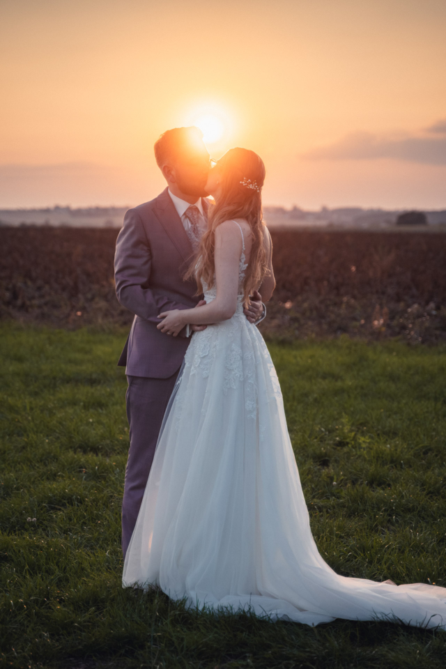 Brautpaar küsst sich bei Sonnenuntergang auf einem Feld