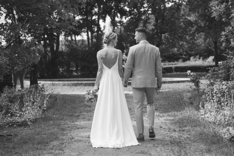 Brautpaar spaziert Hand in Hand durch einen Park